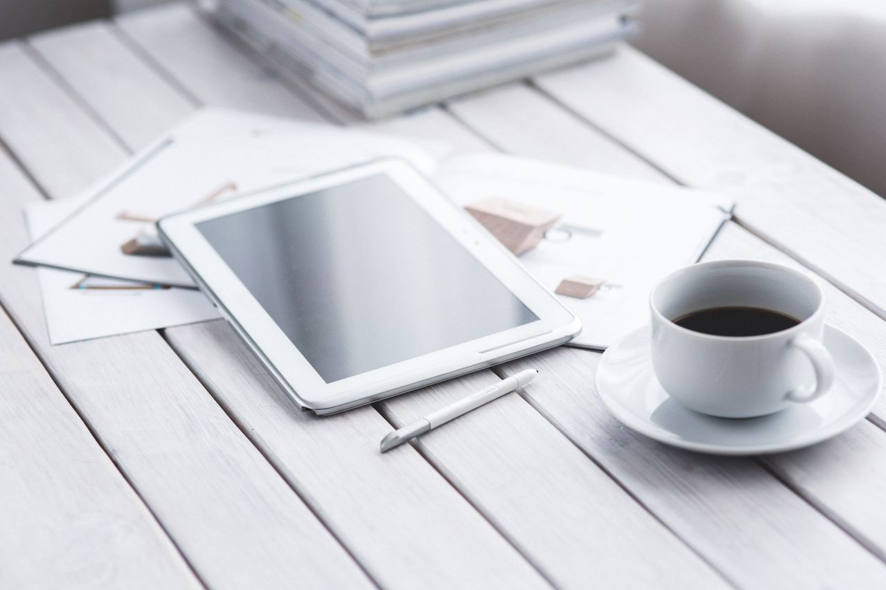 hero-img-01 White tablet with stylus and coffee cup on modern office desk setup.