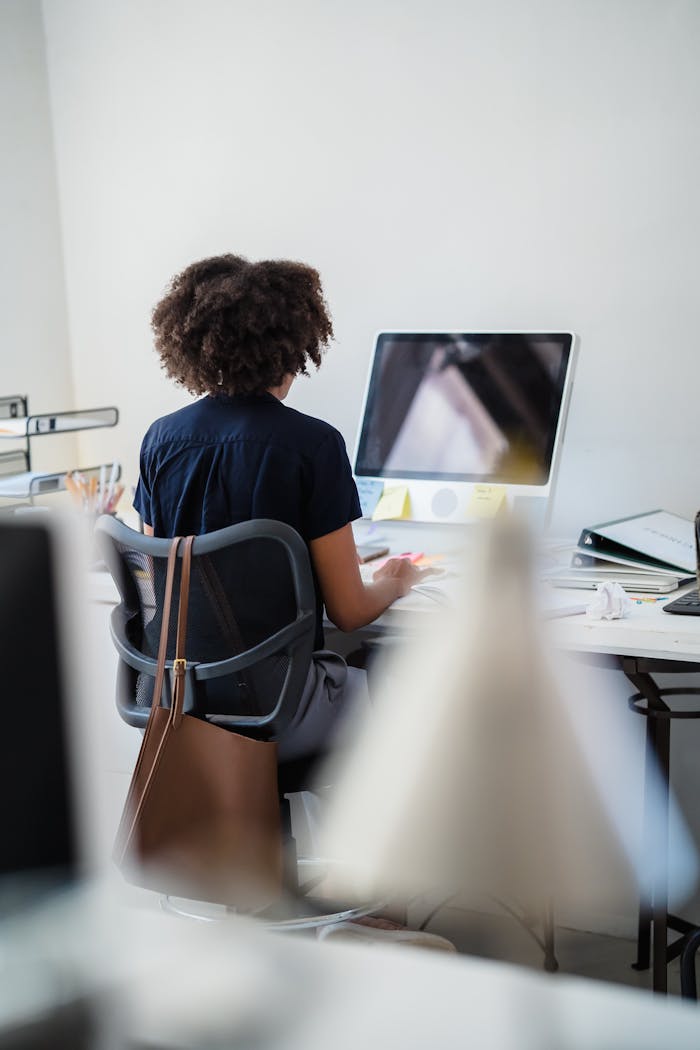 about-01 A woman with curly hair concentrates on computer work at an office desk.