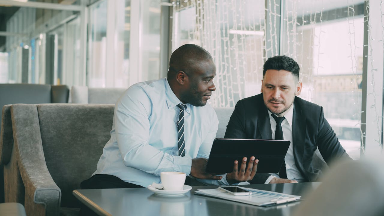 services-img Two men in business attire collaborating over a tablet in a modern office setting.