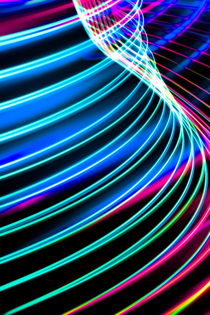 services-02 Dynamic abstract image of neon light trails creating colorful curved patterns over a dark backdrop.