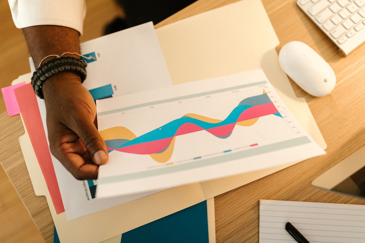 services-02 A person's hand holds a printed business graph paper on a desk with office supplies.